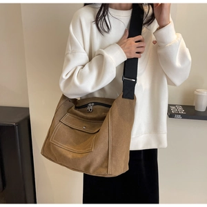 Detail of a brown canvas crossbody bag featuring contrast stitching and a front snap pocket