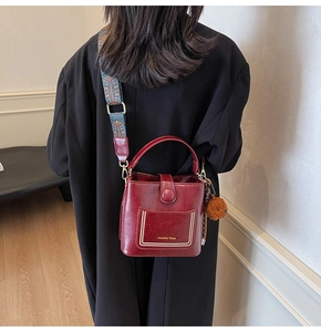 Details einer burgunderroten Beuteltasche mit Vintage-Gurt und Bärenanhänger am Model