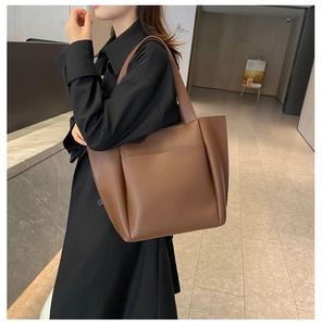 Close-up of brown leather tote bag with a front pocket and soft pleated details on the side