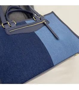 Close-up of denim patchwork tote bag with gold zippers and blue leather handles