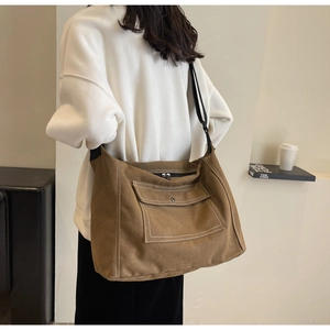 Brown canvas messenger bag with contrast white stitching shown worn by model on shoulder