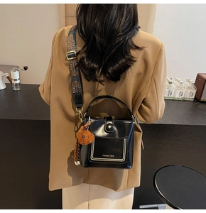 Detail der schwarzen Lackleder-Beuteltasche mit breitem Ethno-Gurt und Plüschbär-Anhänger