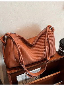 Caramel brown pleated tote bag with double straps on a wooden rack in a lifestyle setting