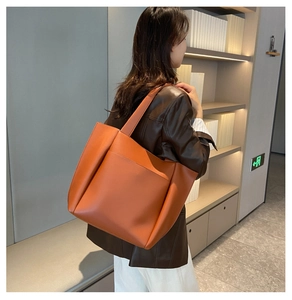 Orange leather tote bag with front pocket shown on a model wearing a brown jacket