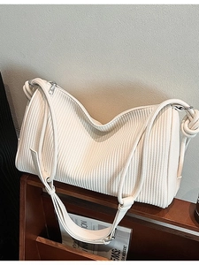 Minimalist beige pleated shoulder bag with knotted strap and silver hardware on wood shelf