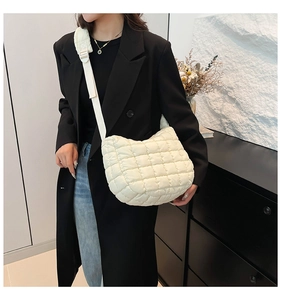 Detail of white quilted nylon crossbody bag with padded shoulder strap against black suit