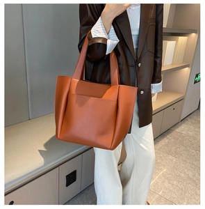 Detail of an orange-red leather tote bag featuring a large front pocket and wide shoulder straps