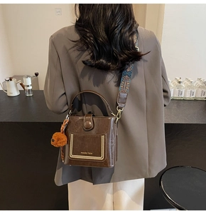 Detail der Retro-Beuteltasche in Braun mit Boho-Gurt und Plüschbär-Anhänger