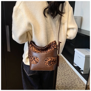 Detail view of leopard print bucket bag with brown leather trim and metal buckles