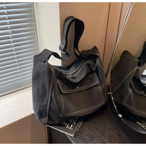 Detail view of black canvas tote bag showing contrast white stitching and front snap pocket