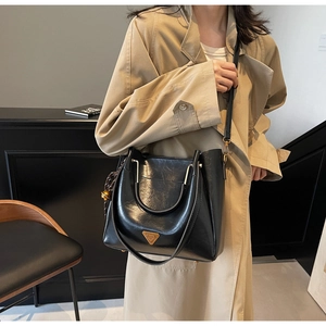 Close-up of black oil wax leather tote bag with metallic logo and tassel charm on a coat