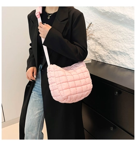 Close-up of pink quilted puffer bag with crossbody strap on a model wearing a black coat