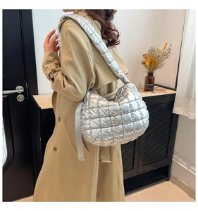 Detail of silver quilted crescent bag with metallic texture on a model wearing a trench coat