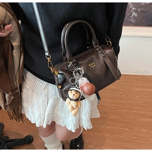 Detail view of brown leather baseball bag with teddy bear charm and gold metal hardware