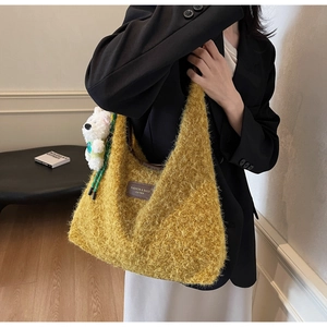 Close-up of yellow plush tote bag featuring a leather brand tag and a cute bear charm