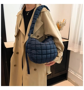 Detail of navy blue quilted puffer bag with adjustable padded strap shown on a model