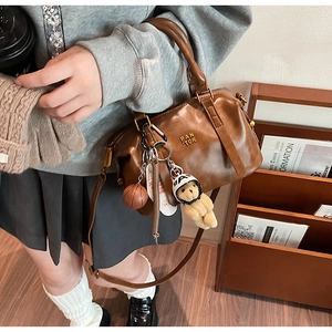 Detail of vintage brown leather baseball bag with plush bear charm and metallic logo