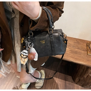 Close-up of black leather baseball bag with gold logo, teddy bear and basketball charms