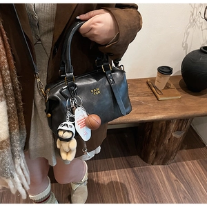 Close-up of black retro baseball bag featuring teddy bear and basketball charms on strap