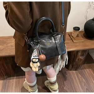 Detail of black matte leather Boston bag with plush bear charm and gold brand logo