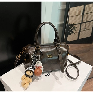 Detail of dark brown leather baseball bag with gold logo, plush bear and mini basketball charms