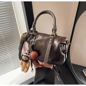 Detail of a brown leather Boston bag with a teddy bear racer and basketball charm