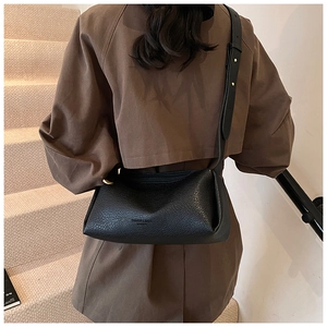 Black lychee texture pillow bag with gold rivet strap worn over a brown coat