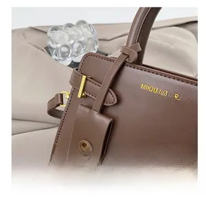Détail montrant la texture du cuir, le logo doré et le pendentif de sac miniature