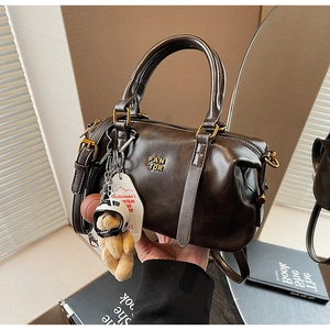 Detail of dark brown vintage Boston bag with gold metal logo and cute bear pendant charm