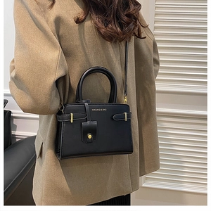 Détail du sac bandoulière noir avec finitions dorées porté par un mannequin en blazer
