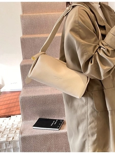 Chic cream-colored leather barrel bag worn with a stylish trench coat in an urban setting