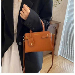 Détail d'un sac bandoulière en cuir marron avec poignée et logo de la marque