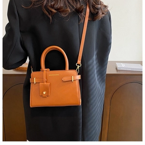 Détail du sac à main marron caramel avec lettrage doré porté sur un blazer noir