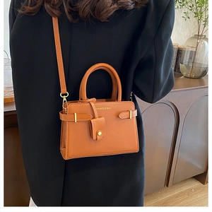 Gros plan du sac bandoulière en cuir marron avec détails dorés et lettrage du logo