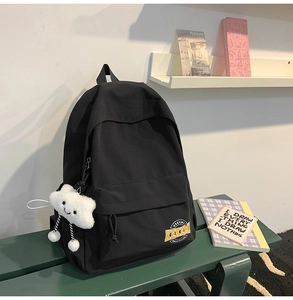Detail of a minimalist black canvas backpack with a cute cloud plush charm attached