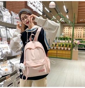 Pink canvas backpack with plush cloud pendant and logo detail in a retail setting