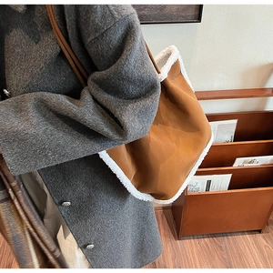 Detail of a large brown suede tote bag with white faux shearling trim and slim leather handles