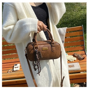 Brown vintage Boston pillow bag with cute charms on a sunny wooden park bench
