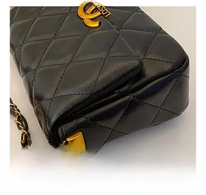 Close-up of black quilted leather texture with gold chain and luxury logo detail
