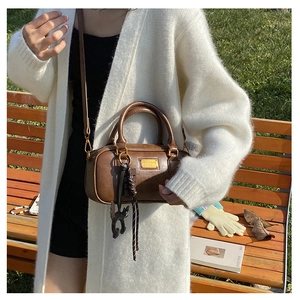 Detail of a brown Boston pillow bag featuring a cat charm on a park bench setting
