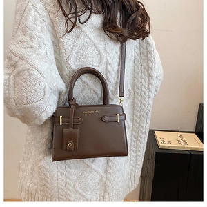 Détail du sac à main en cuir marron foncé avec logo doré porté par le mannequin