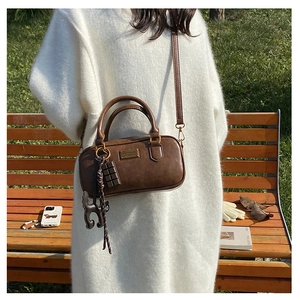 Detail of vintage brown Boston pillow bag with golden plate and cute pendants on park bench