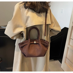 Detail einer braunen matten Wildleder-Tote-Bag mit Metallschnallen am beigen Trenchcoat