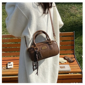 Brown leather Boston bag with gold hardware and charms shown in a park setting