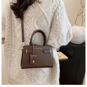 Sac bandoulière en cuir marron foncé avec boucle métallique dorée sur la sangle