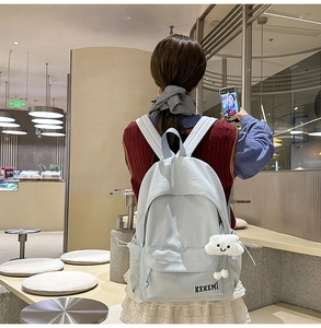 Rear view of model wearing a light blue nylon backpack with a fluffy cloud pendant accessory