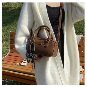 Detail of a brown Boston bag featuring a metal nameplate and cute chocolate cat charms