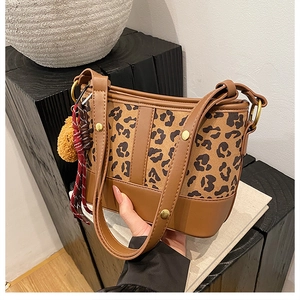 Detail of leopard print bucket bag with golden studs and colorful pom-pom accessory