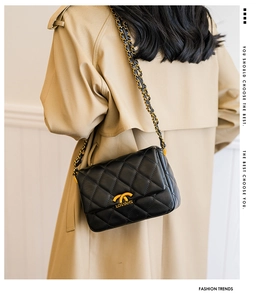 Detail of black quilted leather shoulder bag with gold chain strap on beige trench coat