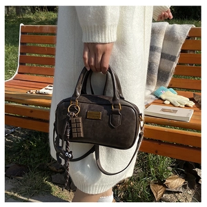 Detail of dark brown Boston bag with cute cat charm and golden plaque in autumn park